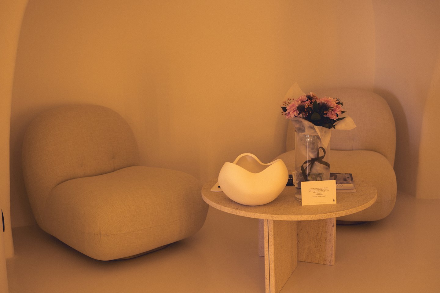 Due poltrone beige circondano un tavolino in pietra con fiori freschi.